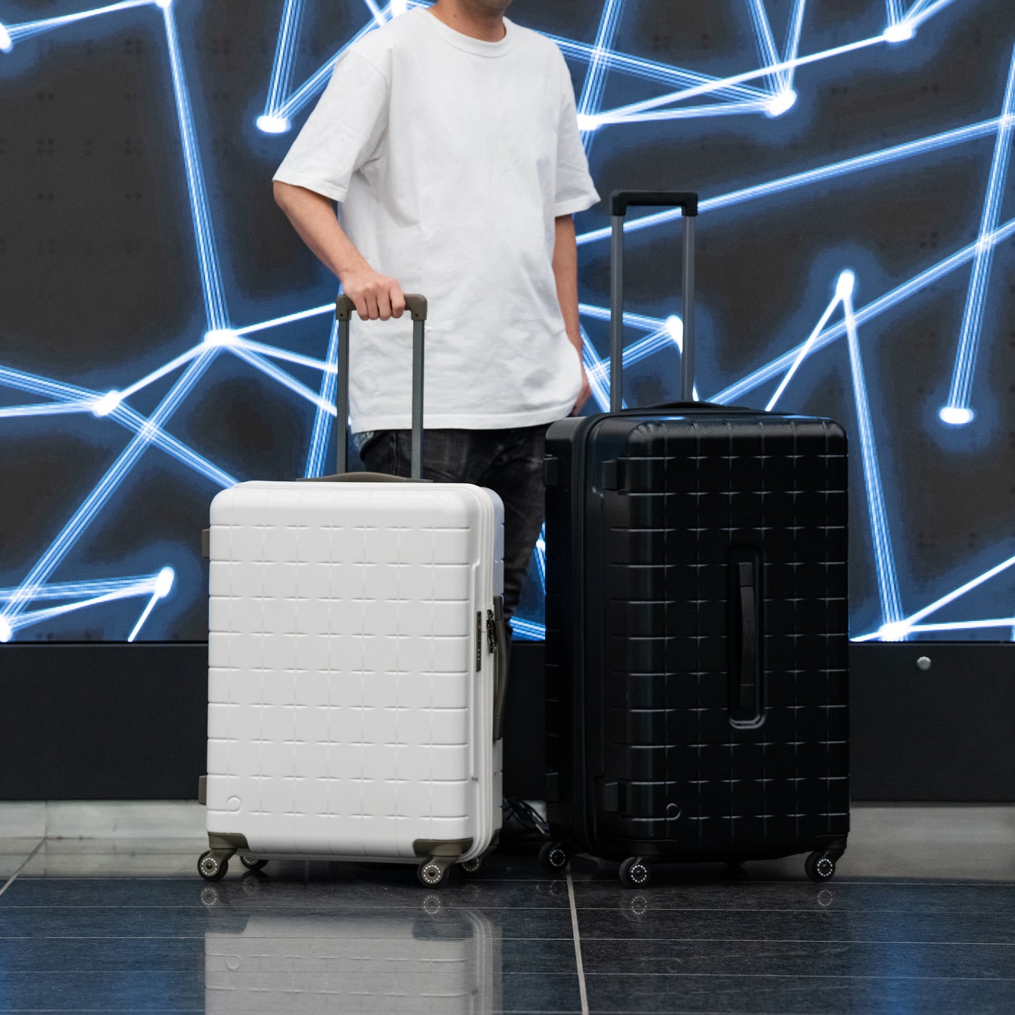 White and black PROTECA 360G4 suitcases shown side by side with traveler for size comparison
