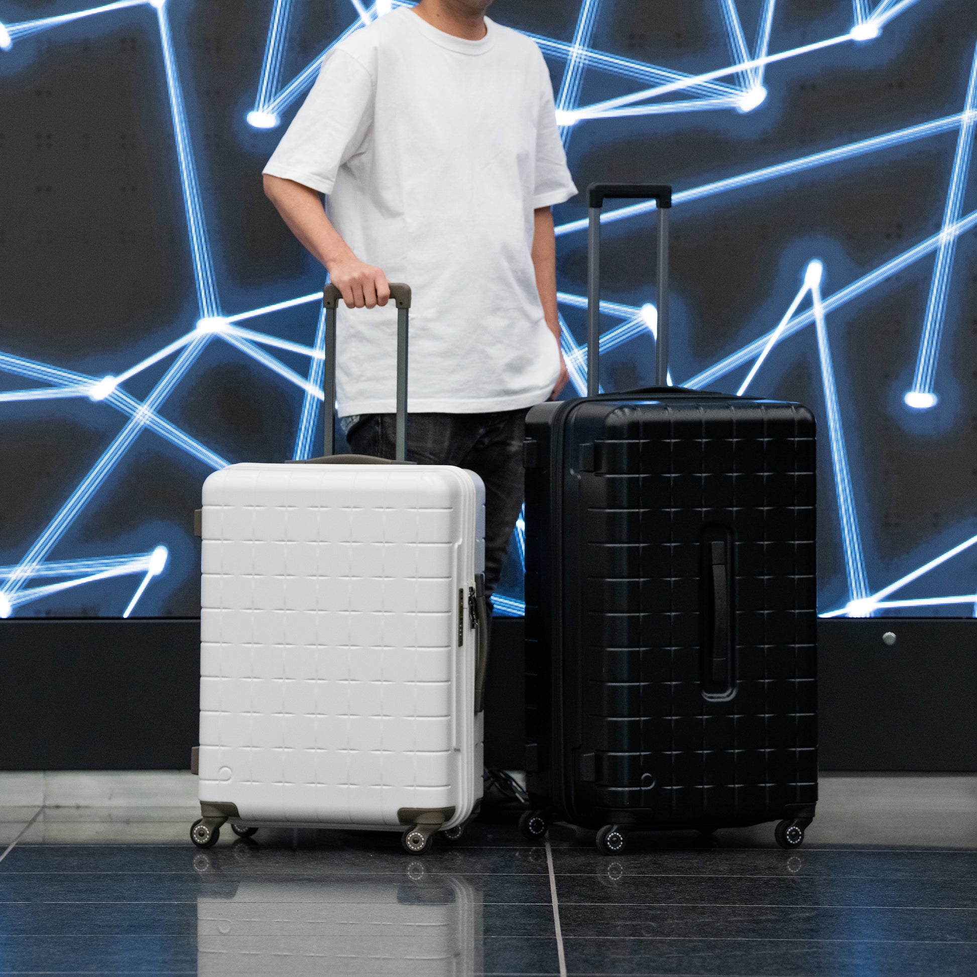 White and black PROTECA 360G4 suitcases shown side by side with traveler for size comparison