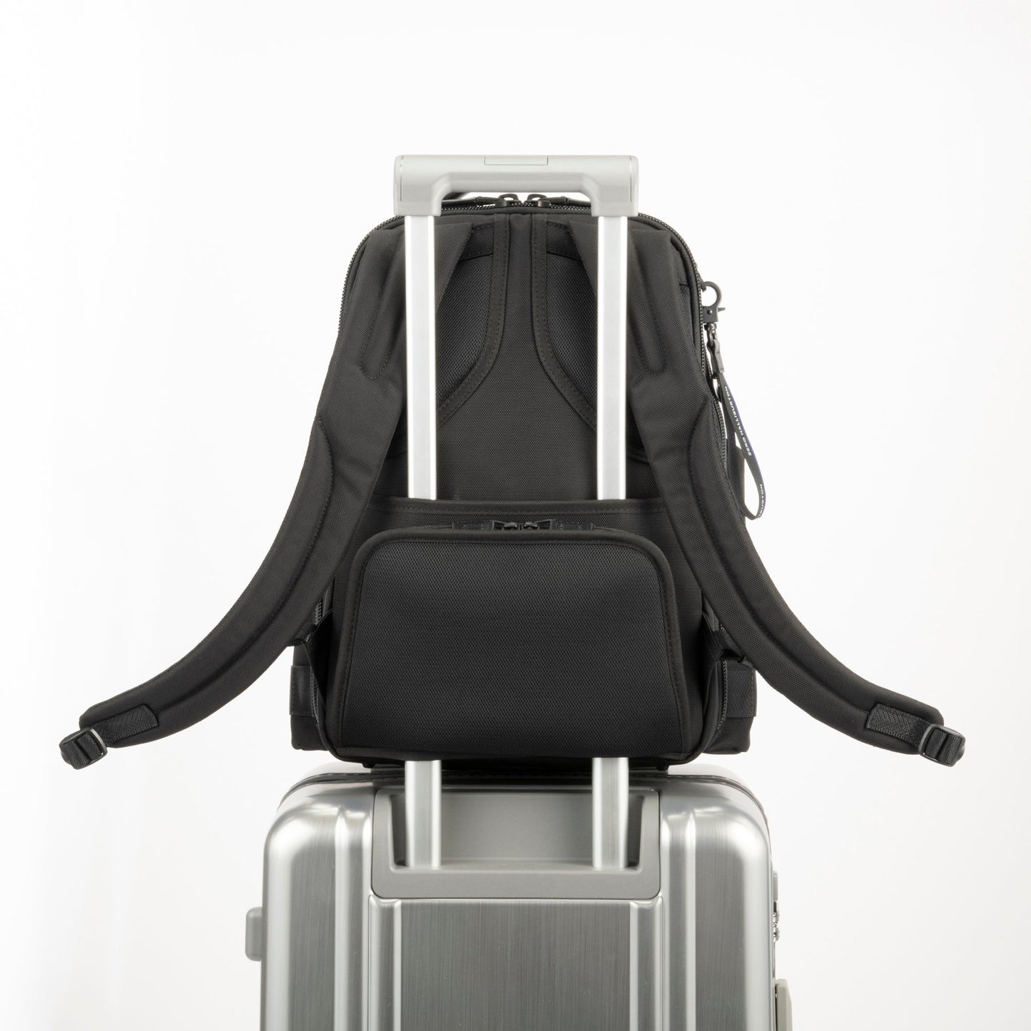 Black - backpack on top of a silver suitcase with a white background