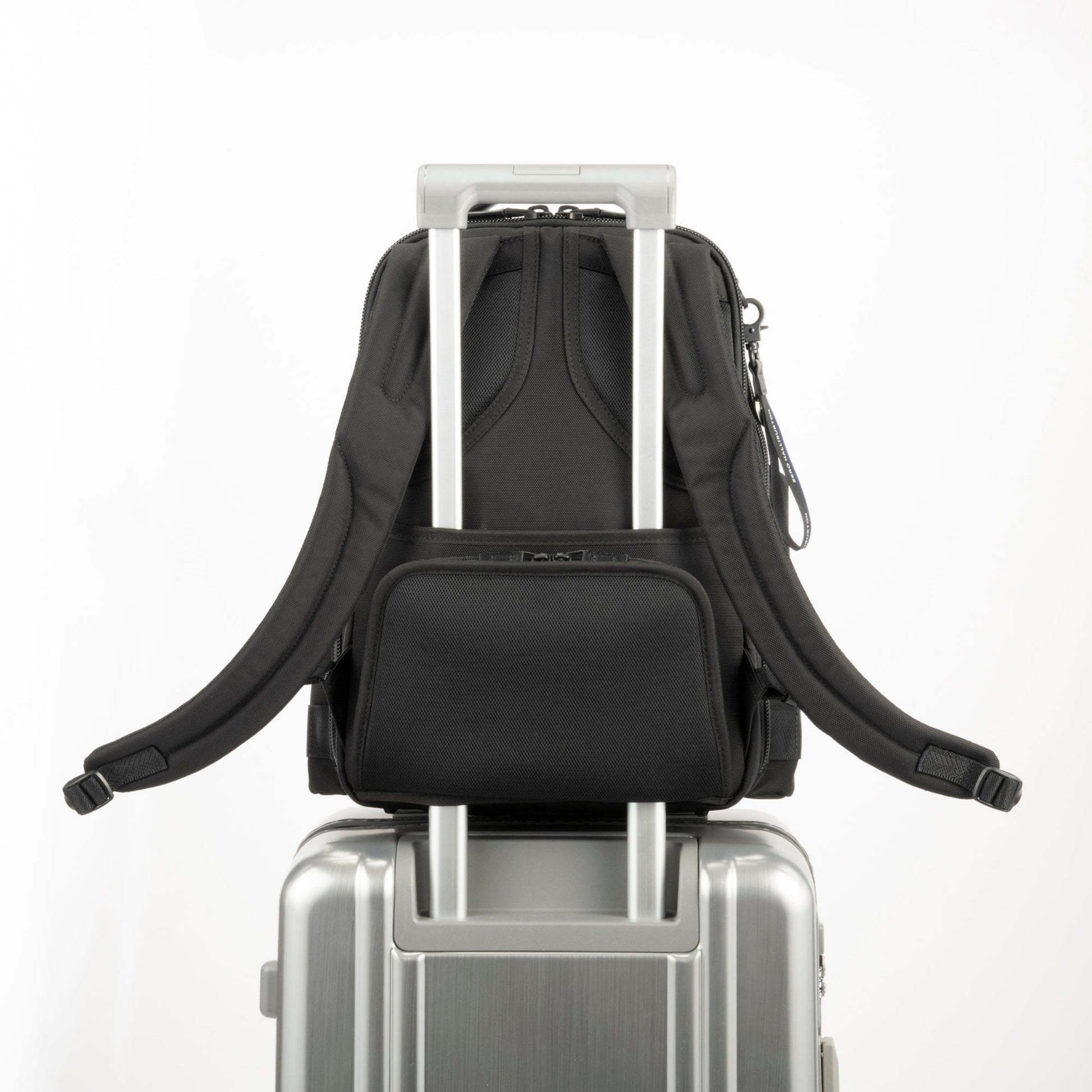 Black - backpack on top of a silver suitcase with a white background