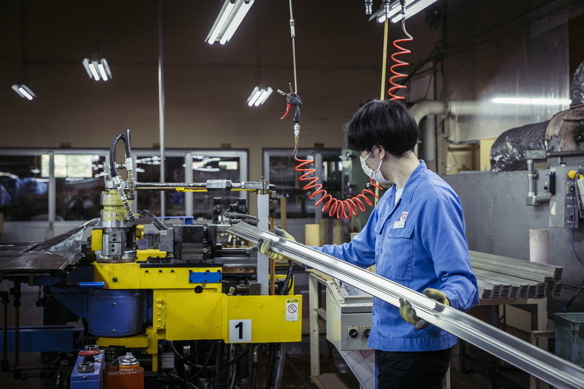 Factory worker operating aluminum frame bending machine in luggage manufacturing facility